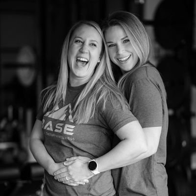 Two women smiling and hugging in a friendly, joyful moment.