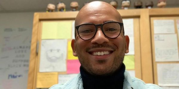 Tyler smiling and wearing glasses in front of student work in his classroom.