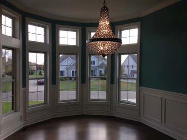 Elegant chandelier in a spacious room with large bay windows overlooking a neighborhood.