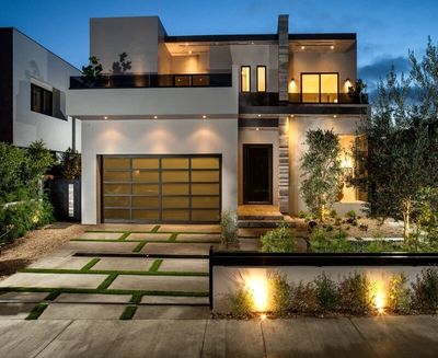 Modern two-story house with illuminated exterior and sleek garage door at dusk.