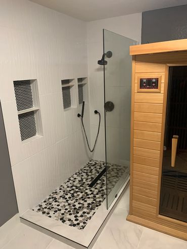 Modern shower area with pebble-style flooring and adjacent wooden sauna.