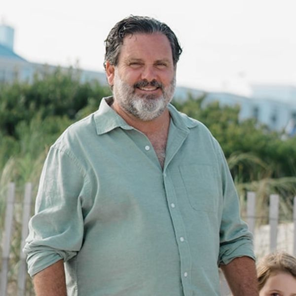 Smiling man with beard wearing a light green shirt outdoors.