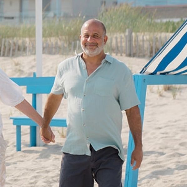 A smiling man holding hands on a sandy beach near blue benches.