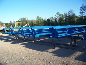 The image shows multiple large, blue, tubular metal structures laid out horizontally on a flat