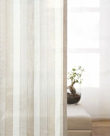 A beige multi-striped drapery panel with a bench and window in the background.