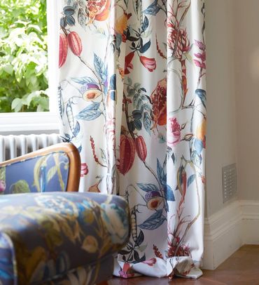 A picture of the bottom portion of colourful floral drapery hanging in a window with an outdoor view