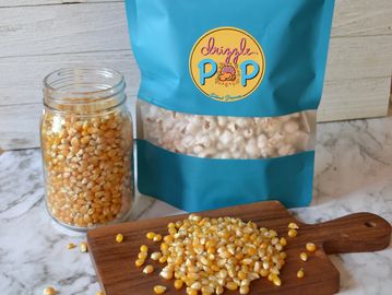 Bag of Drizzly Pop popcorn with kernels in jar and on wooden board.