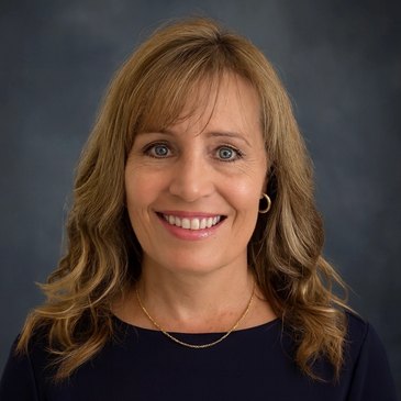 Smiling woman with wavy blonde hair and blue eyes against a dark background.