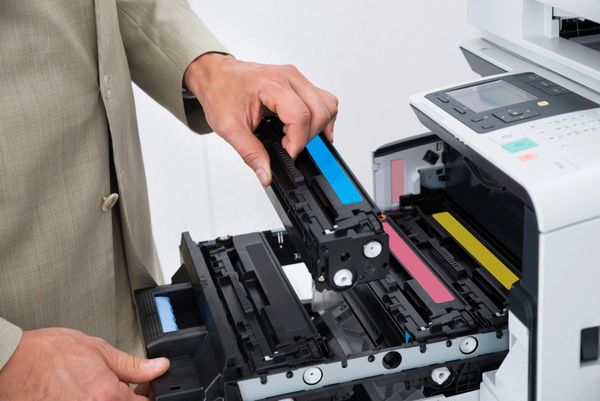 A person in a beige suit installs a blue toner cartridge into a printer