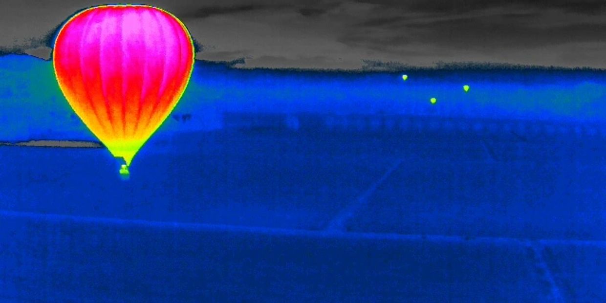 Thermal image of a hot air balloon glowing warmly against a cool landscape.