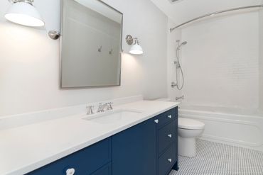 Modern bathroom with blue vanity and white bathtub.