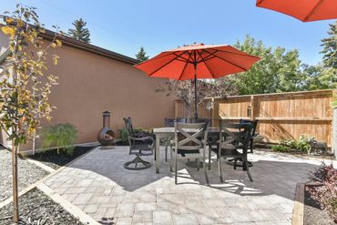 Outdoor patio with table, chairs, and orange umbrella in a backyard.