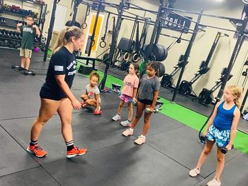 A trainer instructs a group of children in a gym setting with exercise equipment.