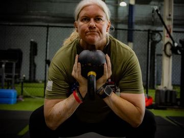 Woman performing a kettlebell squat in a gym.