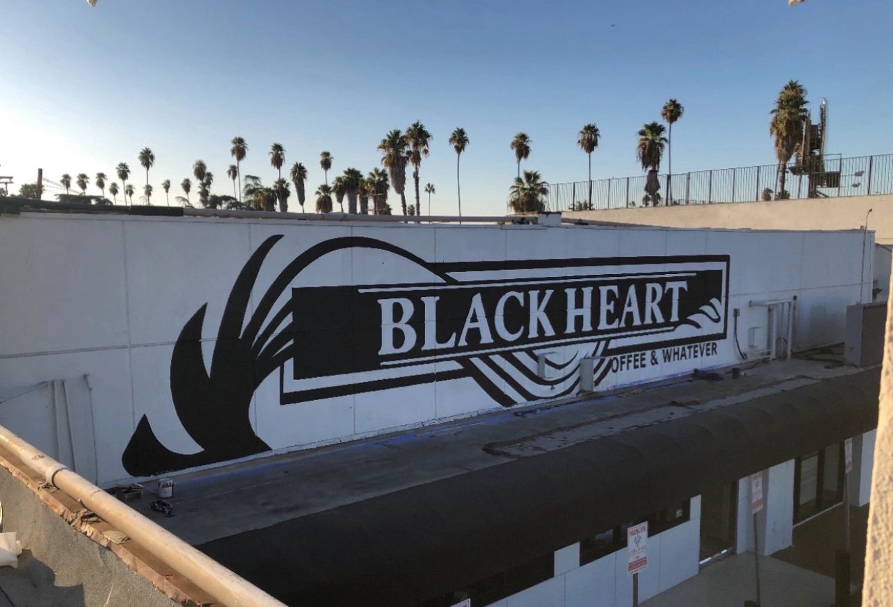 Black Heart coffee shop mural on a building wall with palm trees in the background.