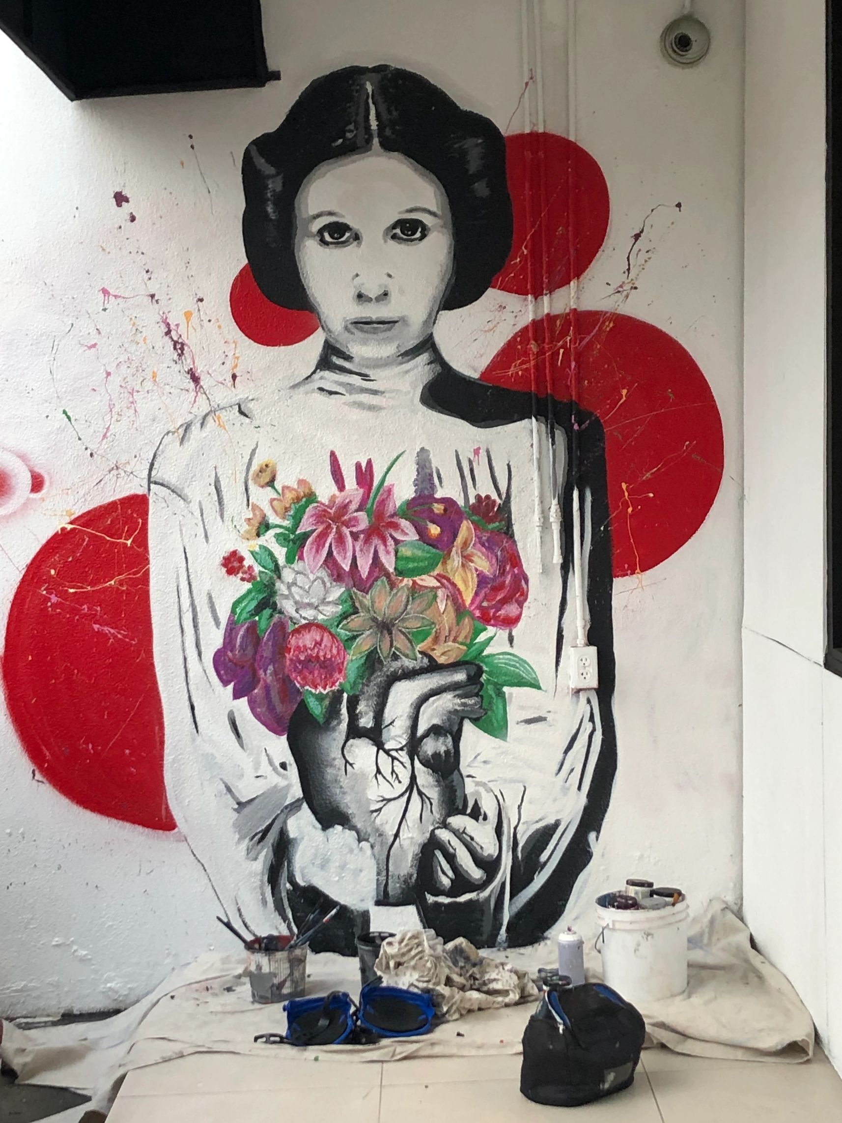 Street art of a woman holding floral bouquet with an anatomical heart and red circles backdrop.