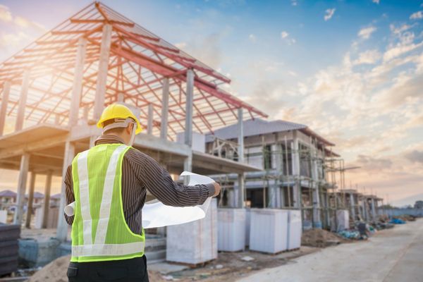 Construction site with engineer holding blueprints and inspecting building framework at sunset