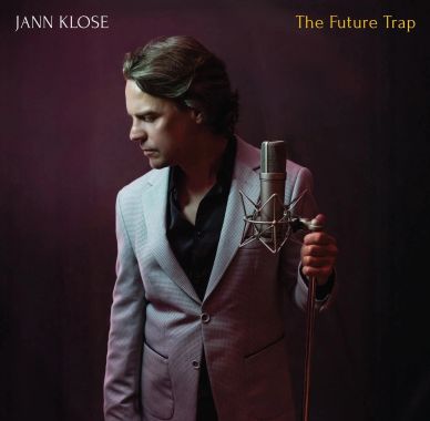 Jann Klose in a contemplative pose holding a microphone against a dark background.