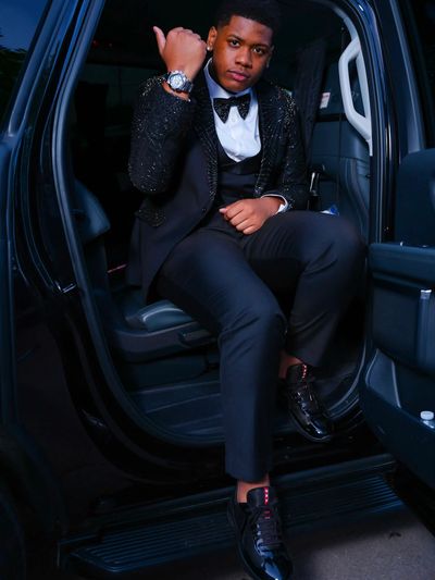 Young man in a black tuxedo posing in a car door.
