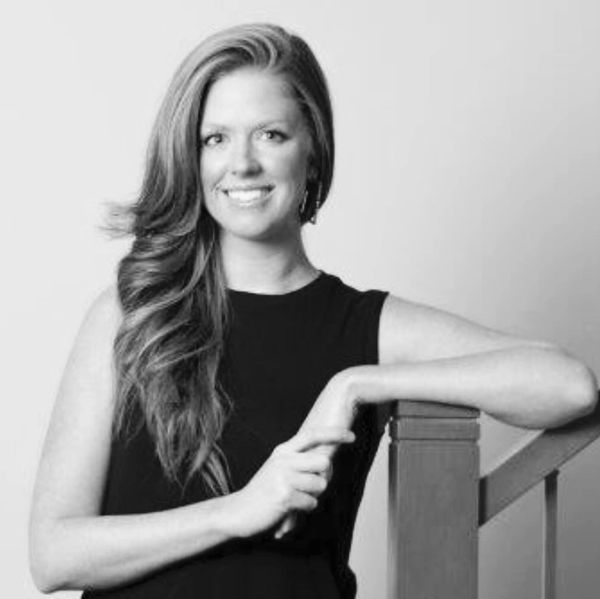 Woman with long hair leaning on a wooden railing, smiling confidently.
