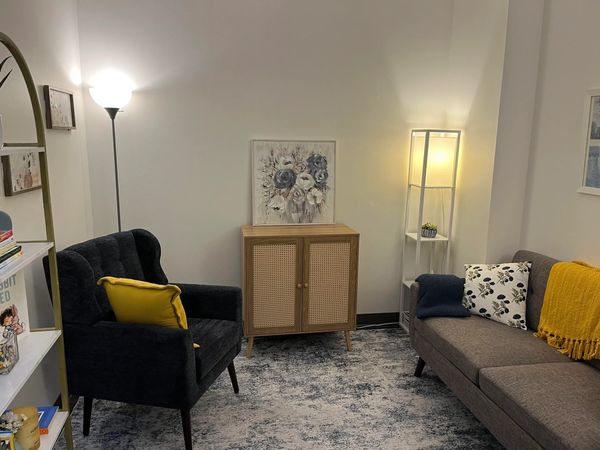 Cozy living room with a dark armchair, gray sofa, and warm lighting for individual therapy or couples therapy. 