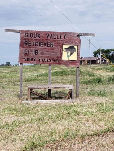 Wooden sign for Sioux Valley Retriever Club in a grassy field with a dog silhouette.