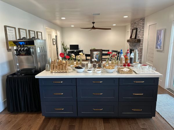 Ice cream sundae bar setup with cones, toppings, and sauces on a kitchen island.