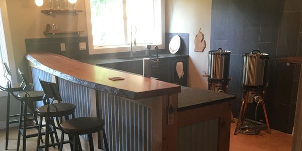 Rustic home bar with wooden stools and brewing equipment.