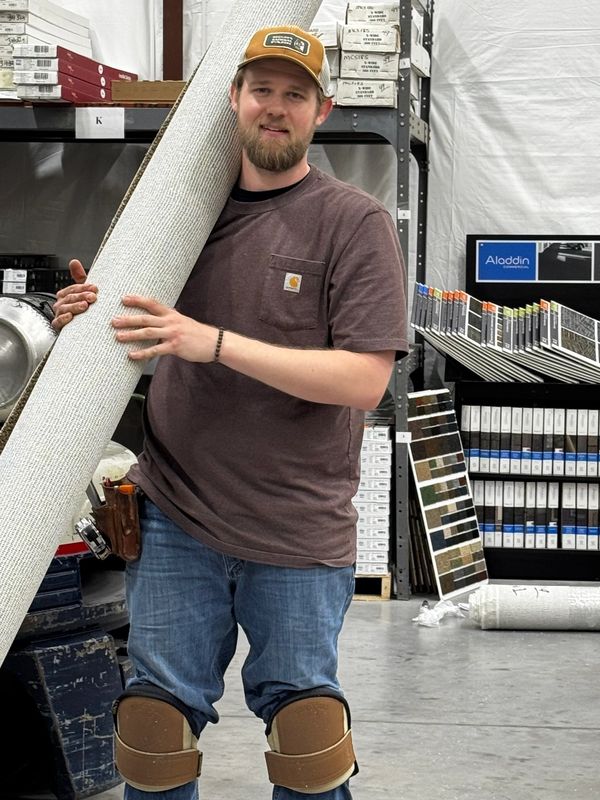 Man holding a carpet roll in a warehouse.