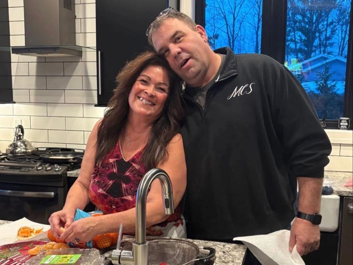 Couple smiling in a kitchen while peeling oranges.
