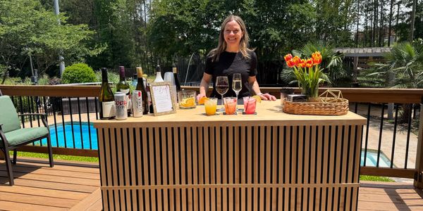 Woman standing behind outdoor bar with drinks and flowers.