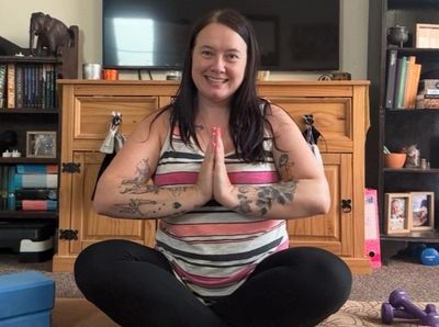 Woman sitting cross-legged smiling with hands in prayer position.