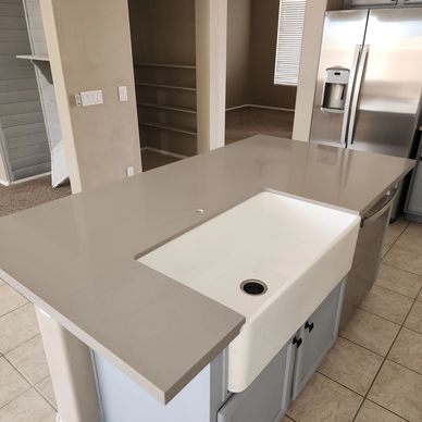 Modern kitchen island with a built-in farmhouse sink and gray countertop.