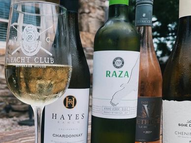 A wine glass and four bottles of wine from different brands on a table outdoors.