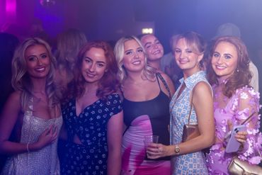 A group of girls dressed up for a party hosted in a nightclub, some are holding drinks in their hand