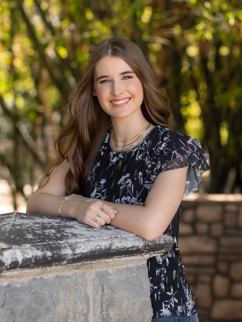 Young woman smiling outdoors, leaning on a stone ledge.