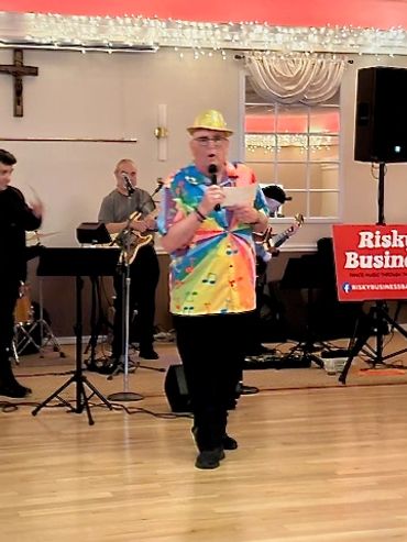 Man in colorful shirt and gold hat speaking on stage with a band.