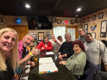 A group of people gathered around a table smiling at the camera indoors.