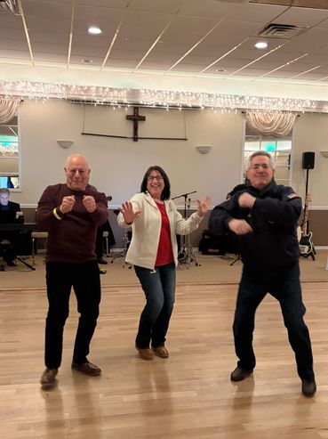 Three adults dancing joyfully in a decorated room with musical instruments.