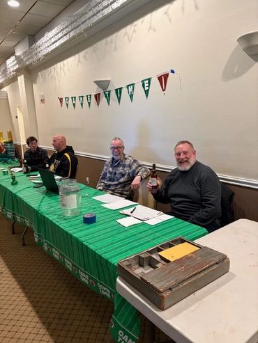 Men sitting at a green-themed welcome table in a room.