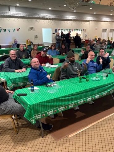 Group of people sitting at tables with green tablecloths in a community event.