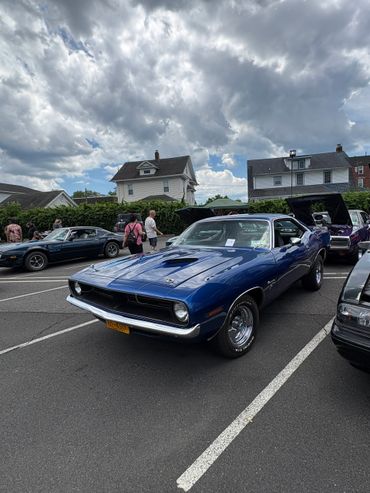 Classic blue muscle car parked at a car show under cloudy skies.