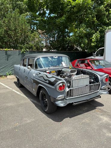 Classic car with exposed engine and flame decals parked outdoors.
