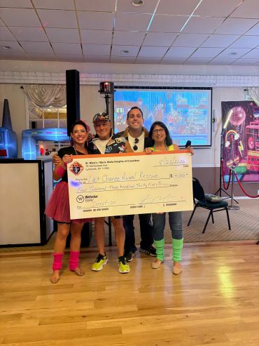 Group of four holding a large donation check indoors.