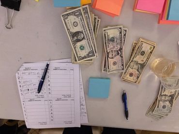 A table with money, pens, sticky notes, and tally sheets.