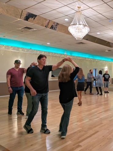 People dancing in a spacious room with chandeliers.