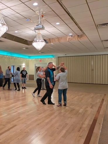 People dancing in a spacious room with chandeliers.