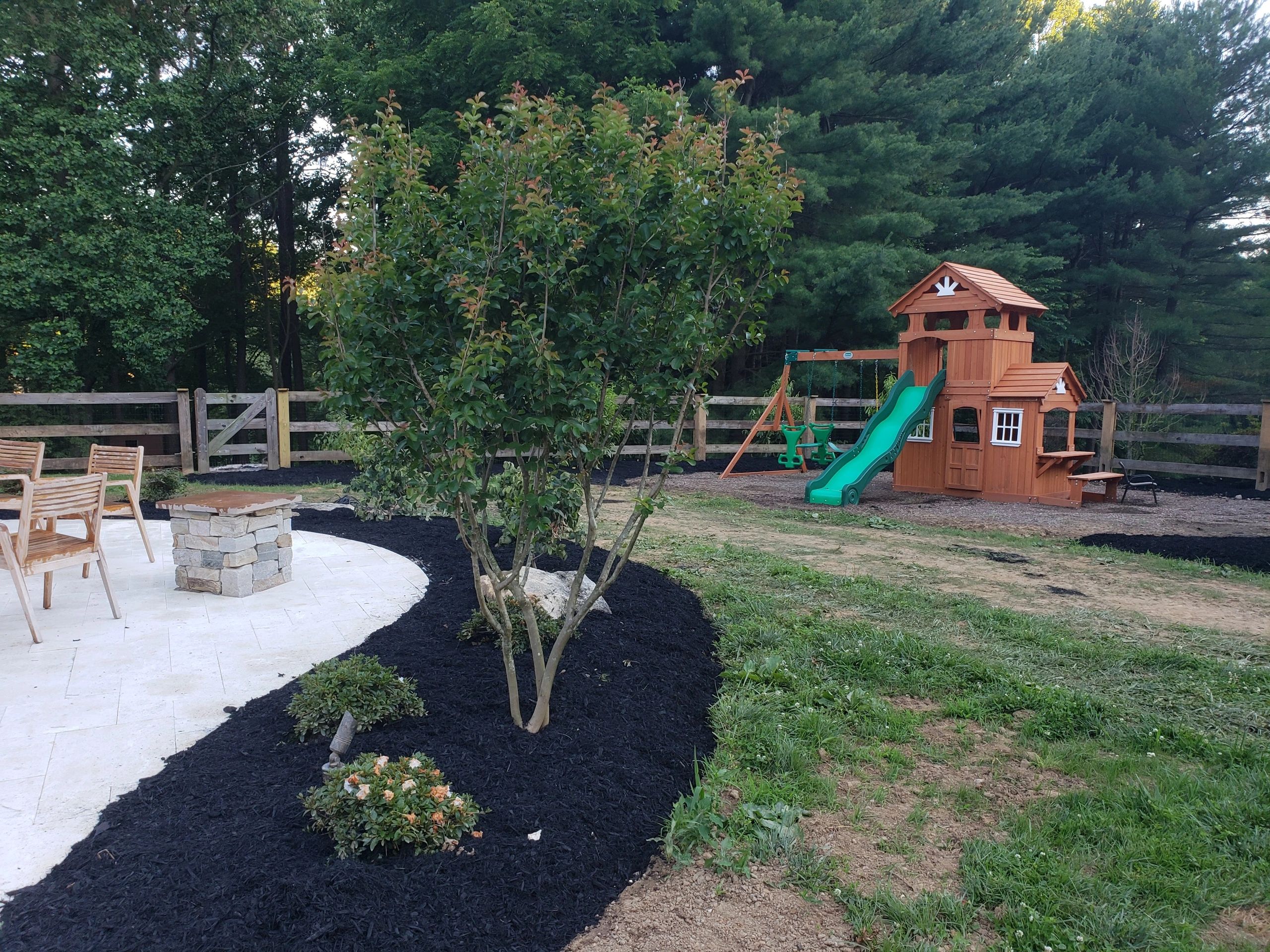 Backyard with a small patio, fire pit, landscaped garden, a wooden playset with a slide and swings.