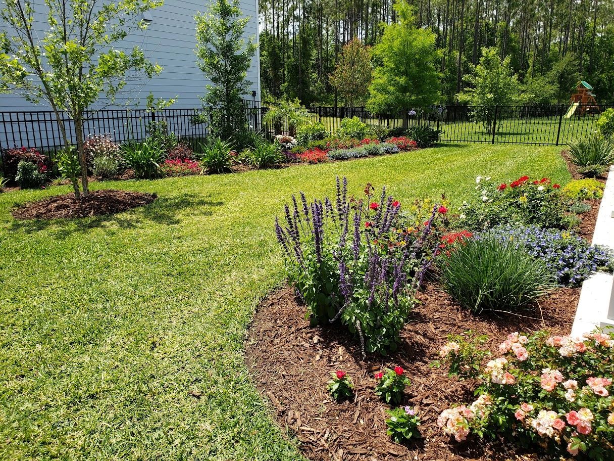 A vibrant backyard garden with colorful flower beds and a neatly manicured lawn, enclosed by a fence