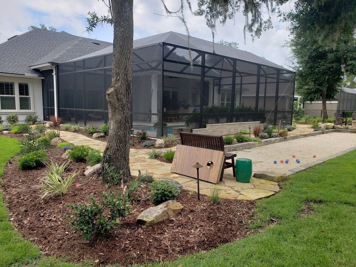 Backyard with a landscaped garden, gravel bocce court, and a large screened-in patio area.